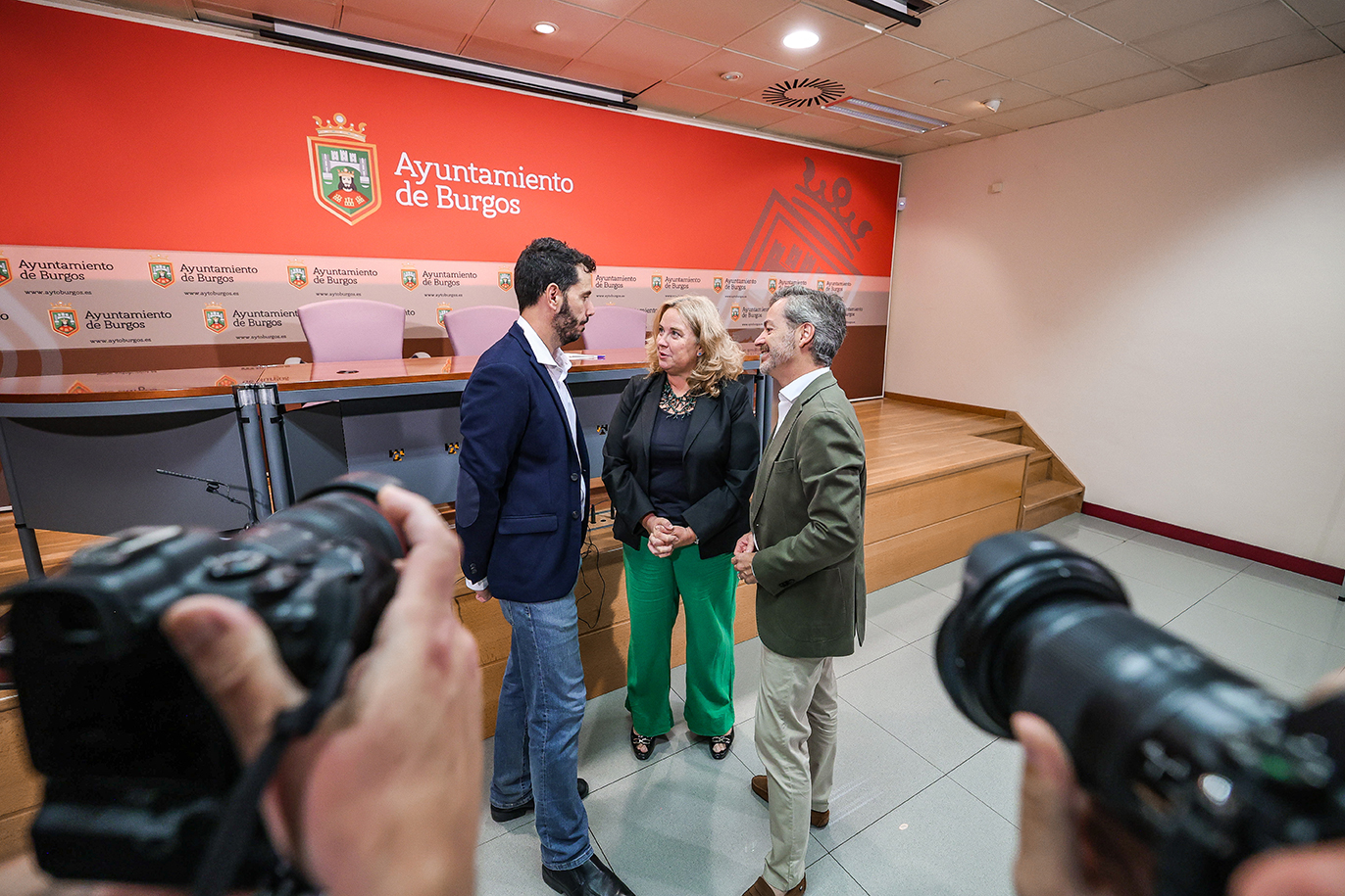 Tres personas conversan en la sala de prensa del Ayuntamiento de Burgos mientras los fotógrafos toman imágenes.